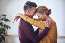 A man and woman share a warm embrace in a dance studio, symbolizing connection and support in their journey with chronic conditions.