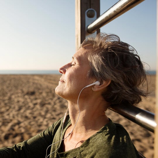 A woman enjoying music on a bench, symbolizing relaxation and support during treatment with Teva-Teriflunomide.