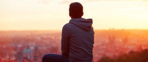 A man relaxes on a ledge, observing the bustling city skyline, immersed in thought and tranquility.