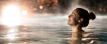 A woman smiles joyfully in the water at night, reflecting her resilience and transformation after battling cancer.