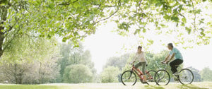 A couple enjoys a leisurely bike ride in a park, promoting fitness and well-being amidst asthma challenges.