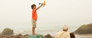 A young boy balances on a box, excitedly playing with a toy airplane, showcasing imaginative play during family activities.