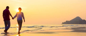 A couple holding hands on the beach at sunset, symbolizing love and resilience after overcoming prostate cancer challenges.