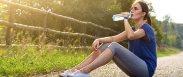 a woman sits on a path and drinks water while resting after a run