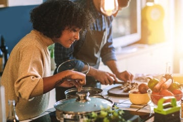 Two people cooking in a sunlit kitchen with fresh vegetables on the counter.