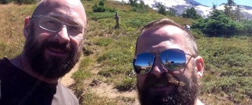 Two bearded men in sunglasses take a selfie, celebrating life after overcoming a heart attack.