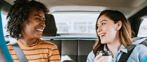 Two passengers in a car, one holding a coffee cup, both wearing seat belts.