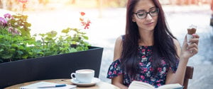 A woman with glasses enjoys a cup of coffee at a table, embracing the joy of solitude amidst her MS journey.