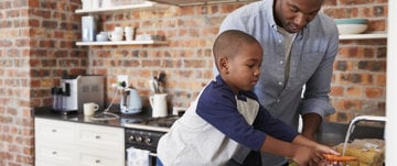 A man and a young boy collaborate in the kitchen, preparing food together, showcasing a moment of shared learning and bonding.