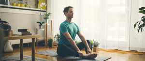 A man sits cross-legged on a mat, practicing yoga, embodying tranquility and focus in a serene environment.