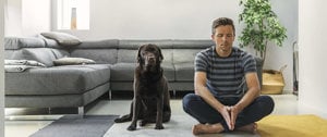 A man is seated on the floor, enjoying the company of his dog, both appearing relaxed and content in their surroundings.