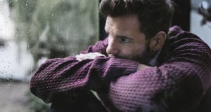 A man stands by a window, looking out contemplatively, embodying a moment of introspection amidst feelings of depression.