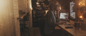 A woman working at a desk with a laptop, implementing techniques to cope with photophobia and migraine at home and work.