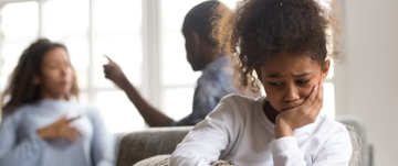 A young girl sits on a couch, hands on her face, reflecting her mental health struggles and desire for understanding from her parents.