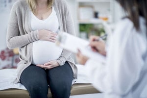 A healthcare professional conducts an examination of a pregnant woman in a medical office.