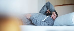 a man in a tracksuit is lying on the couch with his hand over his head