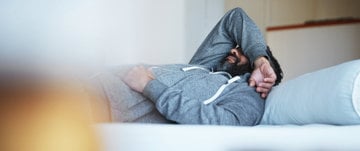 a man in a tracksuit is lying on the couch with his hand over his head