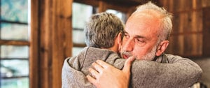 An older man hugs another man, representing emotional support and connection in times of depression crisis.