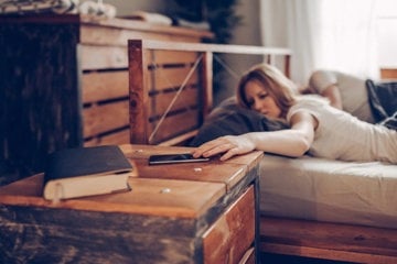 A woman lies on her bed, engaged with her phone, contemplating her strange migraine warning signs.