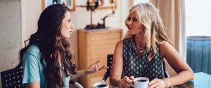 two women are talking and drinking coffee