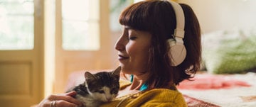 the girl on the couch listens to music on headphones and rests by petting the cat