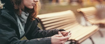 A woman sits on a bench, absorbed in her phone, reflecting on managing social media amid depression and anxiety.