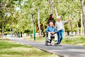 An elderly man and woman in wheelchairs gesture towards an object, highlighting the connection between caregivers and those they assist.