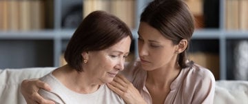 A heartfelt moment as a woman hugs her mother on a couch, symbolizing love amidst the struggle of forgetting names.