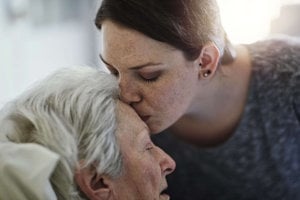 A woman tenderly kisses an elderly woman on the forehead, symbolizing love and care in caregiving relationships.