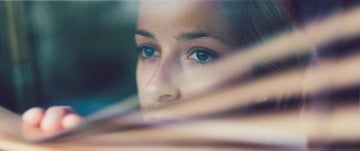 A woman looks out the window, her expression serene, as she observes the world outside in quiet reflection.