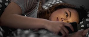 A woman lying in bed, absorbed in her cell phone, reflecting the impact of social media on anxiety levels.