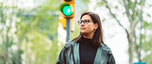 Person in a green jacket standing before a traffic light showing green.