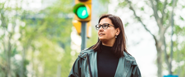 Person in a green jacket standing before a traffic light showing green.