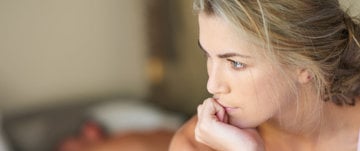 the woman sits on the bed and looks into the distance with her head resting on her hand