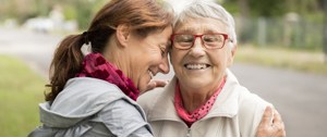 Two older women embrace warmly, symbolizing love and support in caring for family and friends.