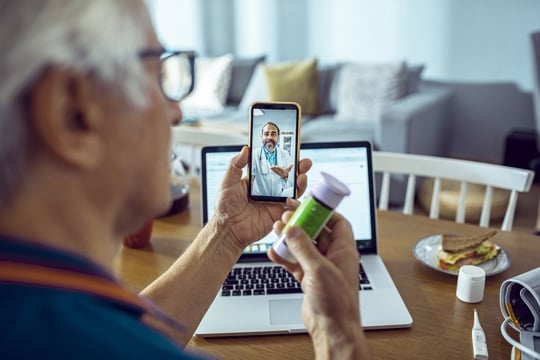 An older man examines a tablet on his device while holding a bottle of pills in his other hand, showcasing health management.