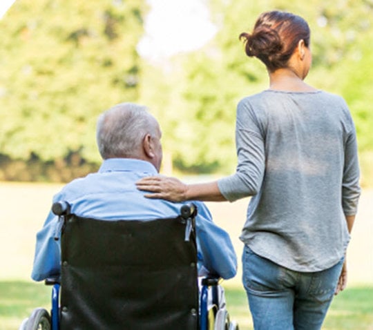 a caregiver walks next to an elderly man in a wheelchair