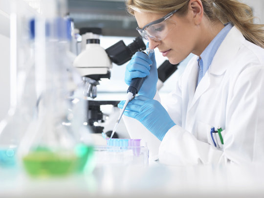 A woman in a lab coat examines a test tube, showcasing her focus and dedication to scientific research.