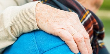 an older woman's hand on an older man's shoulder