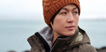 a young Asian woman with a cap on her head is looking away