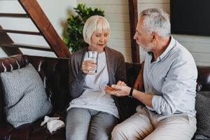 An elderly couple sits comfortably on a couch, holding a glass of water, symbolizing the importance of good medication habits.