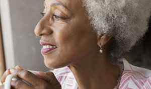 A senior woman with white hair gently holds a cup, reflecting a moment of tranquility and grace.