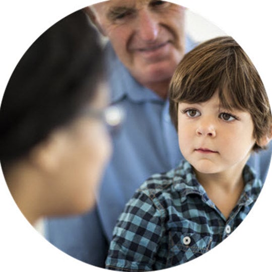 A young boy looks attentively at an older man and woman, representing the value of family and caregiver relationships.