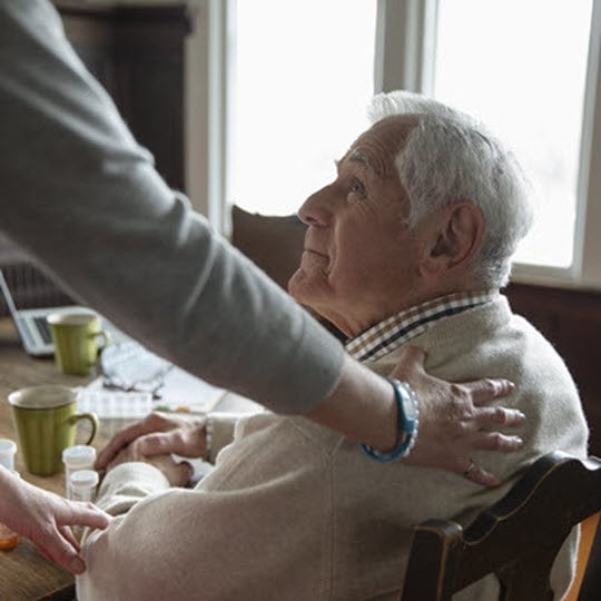 A woman assists an elderly man in taking his medication, showcasing care and support in a compassionate setting.