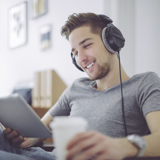 A focused man wearing headphones, engaged with a tablet, showcasing modern technology use.