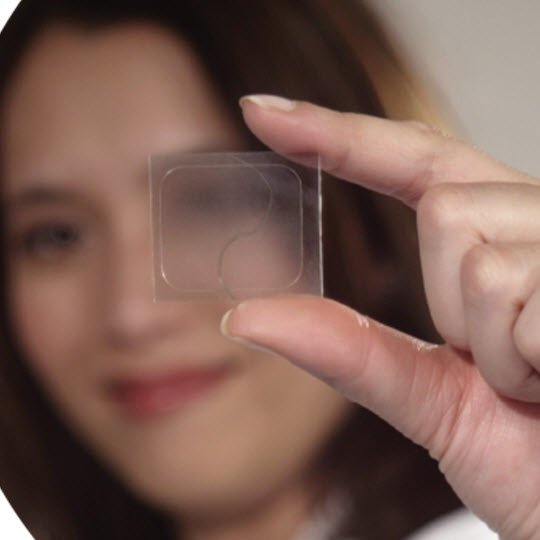 A woman displaying a small square of plastic, showcasing its size and texture with a focused expression.